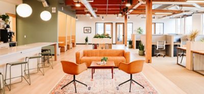 Coworking space with while countertops, a leather sofa and two bucket chairs, and modular cubicles.