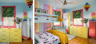A colorful child’s room with light blue walls and bunk bed, yellow-green dresser and wardrobe, rainbow accent wall and details, and wood floor.
