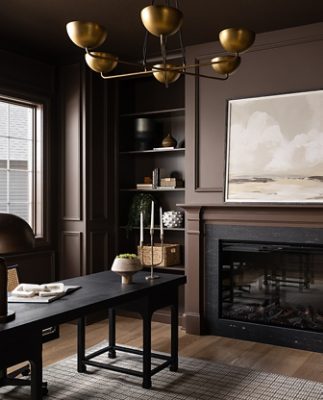 Dark, warmly lit home office with a central fireplace, large landscape painting above the mantel, tall windows, built-in shelving, a desk, green chair, and walls painted Chateau Brown.