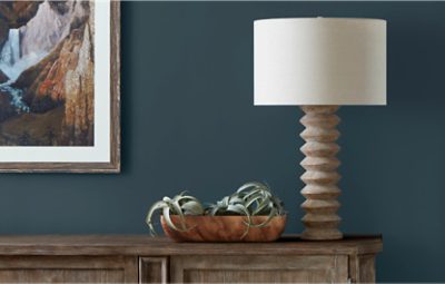 Walls painted in dark blue with a painting on the wall, table and lamp.