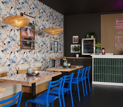 A café interior with blue chairs, wooden tables, floral wallpaper, and a green tiled bar. 