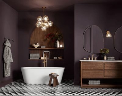 Bathroom walls painted in SW 6272 Plum Brown with wooden shelving with decor on it and a bathtub with gold hardware, wooden vanity with mirrors above it.