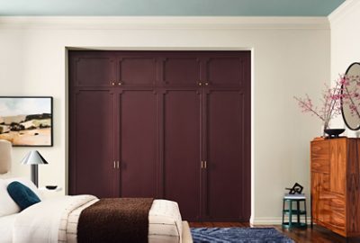 A stylish bedroom with a bed, walls painted Sherwin-Williams White Duck, closet doors painted Cordovan, and a light blue ceiling in the color Quietude.