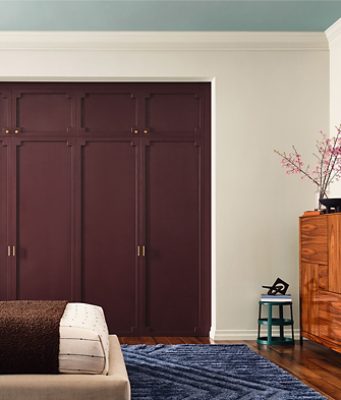A stylish bedroom with a bed, walls painted Sherwin-Williams White Duck, closet doors painted Cordovan, and a light blue ceiling in the color Quietude.