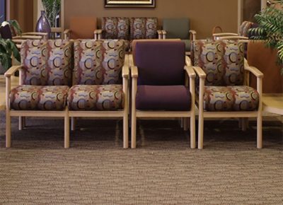 An office waiting room with patterned carpet and chairs and plants.