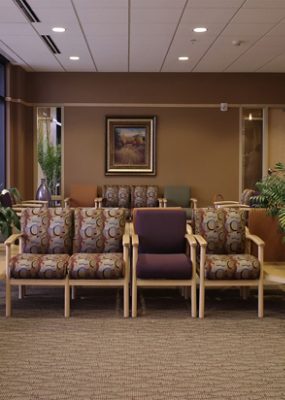 An office waiting room with patterned carpet and chairs and plants.