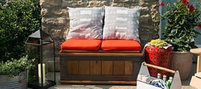An outdoor wooden bench with orange pillows.