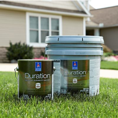 Two containers of Duration paint sitting in the grassy front yard of a house.