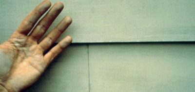 A hand in front of exterior home siding that has paint chalking issues.