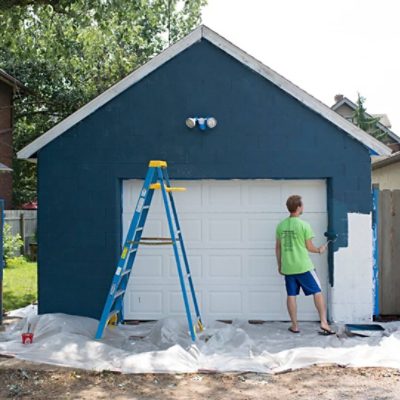 A man painting the trim and edges of a dark blue garage