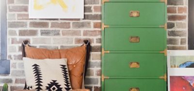 A green laminate dresser in front of a brick wall, leather chair, and wall prints