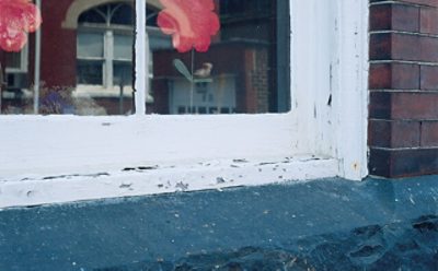 An outdoor windowsill with white paint peeling.