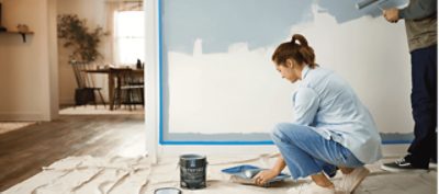 People painting a wall with a roller and Emerald paint.