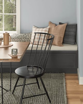 A breakfast nook with a black wooden chair and table with a bench with pillows.