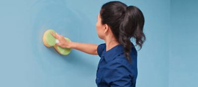 A person scrubbing a painted wall with a sponge.