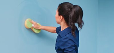A person scrubbing a painted wall with a sponge.