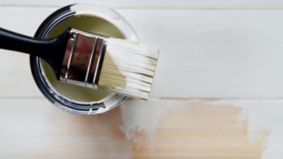 Paint can of cream paint with a paint brush resting on top of it.