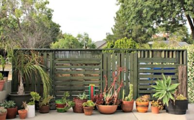 A green painted pallet wall with plants and flowers.