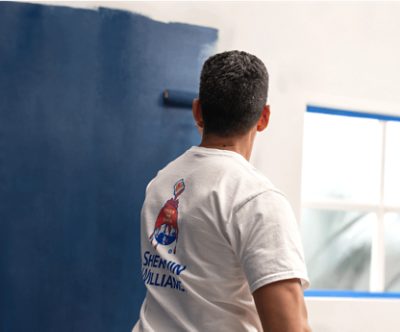 A painter rolling blue paint onto a white wall.