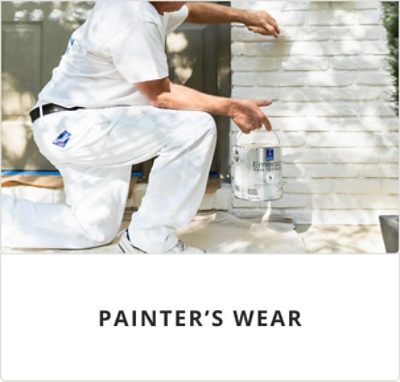 Painter's wear. A person in white painter pants and a white shirt kneeling painting white brick outside.