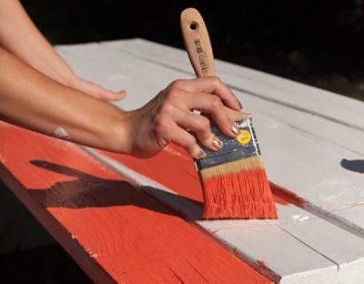 A woman painting a burnt orange picnic table 