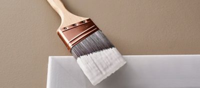 A closeup of a paintbrush with paint on the tip next to wall trim.