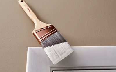 A paint brush with white paint to paint trim.