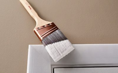 A paint brush dipped in white paint for painting trim. 