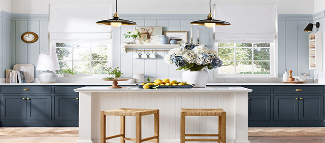 Pottery Barn kitchen walls painted in Upward SW 6239,  two windows, dark cabinets, an island with two wooden stools, and two hanging light fixtures above it.
