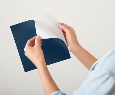 A person peeling the backing off a peel and stick color sample.