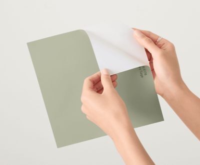 Hands peeling back the top layer of a large green paint sample sheet to reveal the adhesive backing.