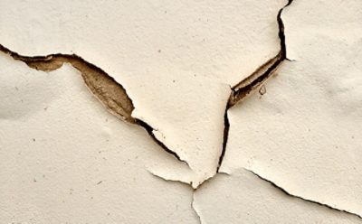A cream colored wall with numerous paint cracks. 
