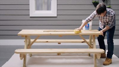 A person wiping a picnic table with a sponge.