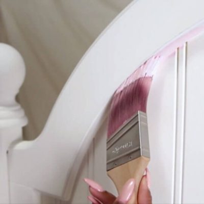 A woman painting a headboard pink 