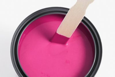 Container of bright pink paint with a wooden stir stick partially submerged, showing freshly mixed paint ready for use.