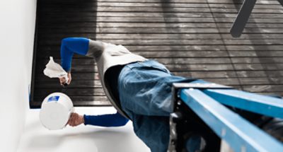 Una persona parada en una escalera sosteniendo un balde de pintura blanca mientras pinta una pared.