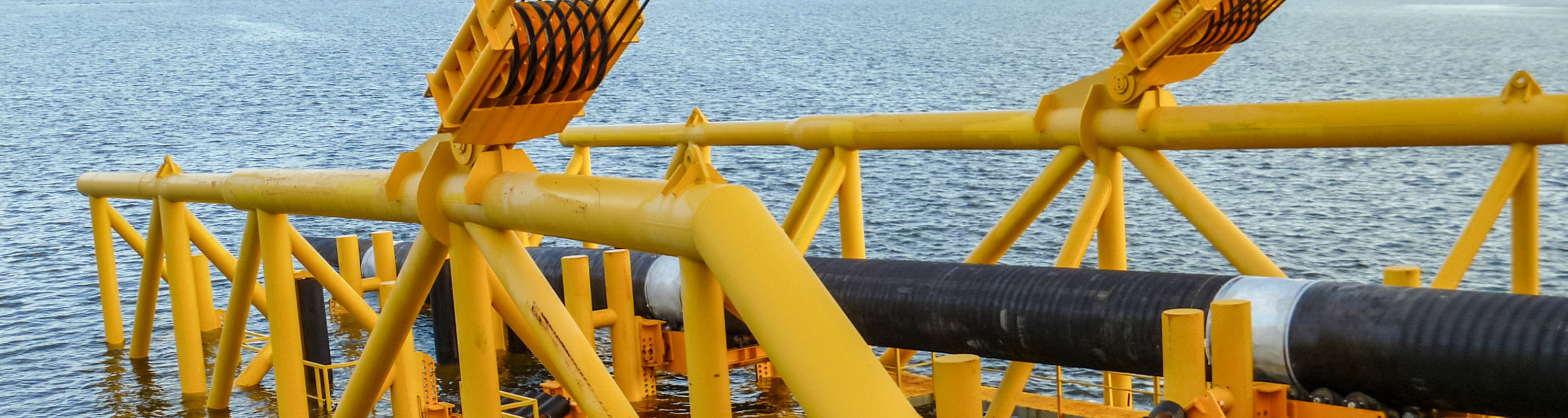 yellow pipe laying barge with stinger lowered laying a black pipe offshore