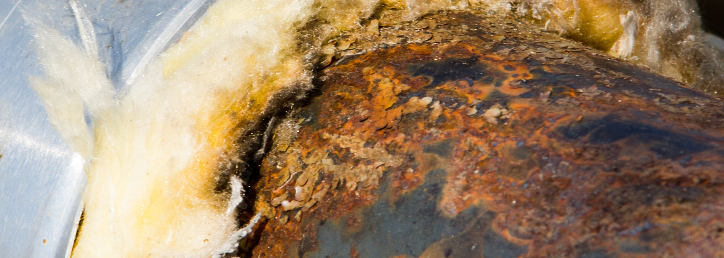 A pipe with the insulation partially removed and showing signs of corrosion under insulation