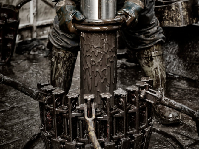 rigworker pulling muddy drill out of earth