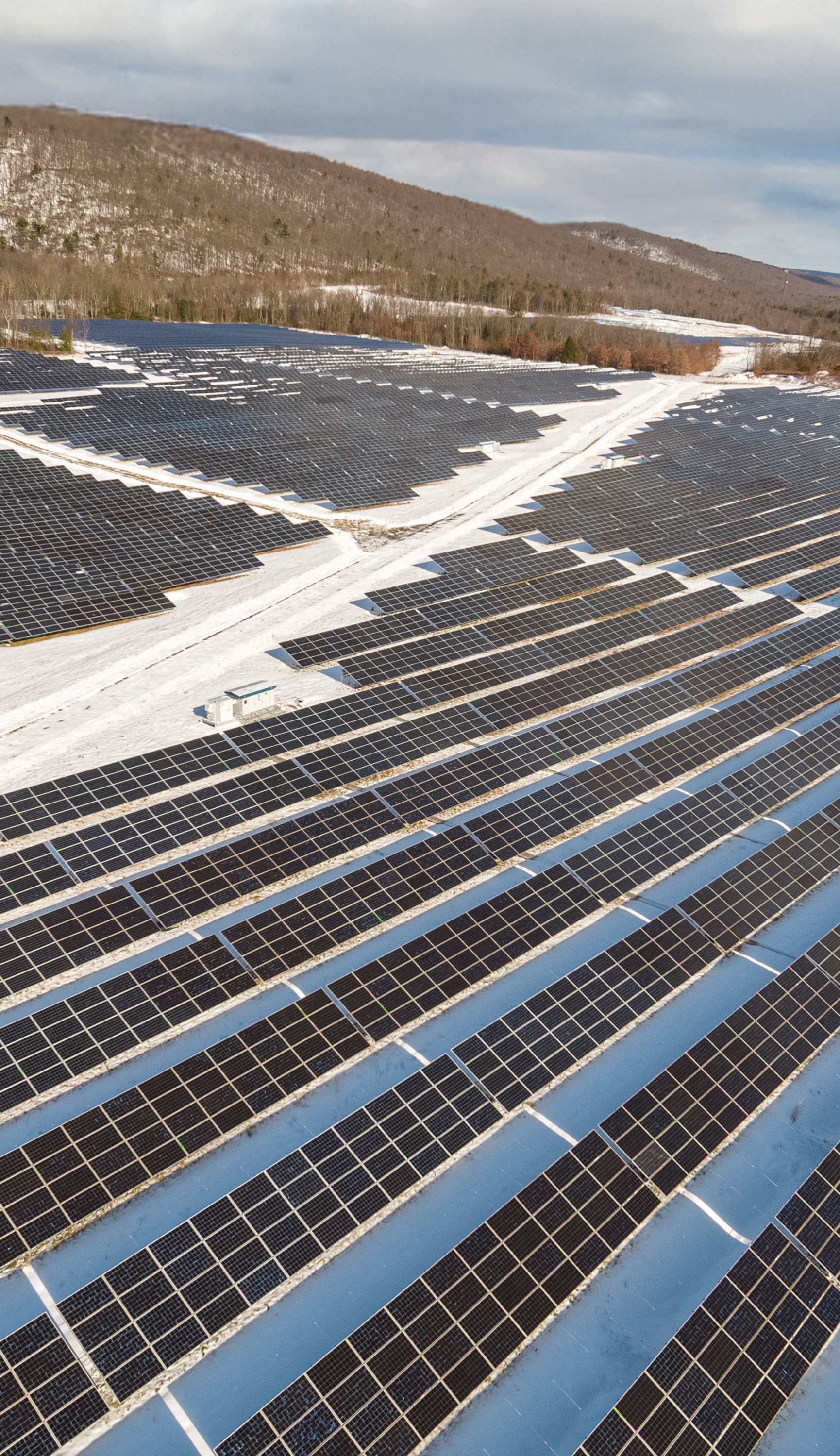 Rows of solar panels installed in a mountainous environment with snow on the ground.