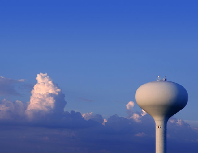 White circular water tower with blue sky and white clouds 