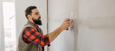 A man sanding a wall in preparation for wallpaper.