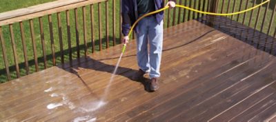 A man rinsing a deck to prepare for staining.