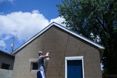A man pressure washing an unpainted garage 