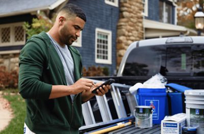 Person standing by a truck on their phone with Sherwin Williams supplies in the truck bed.