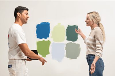 Two people standing in front of a blank wall with six different color swatches.