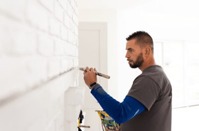 A painter brushing white paint onto a brick wall.