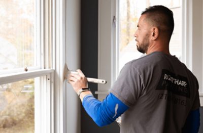 A person painting a white window trim.