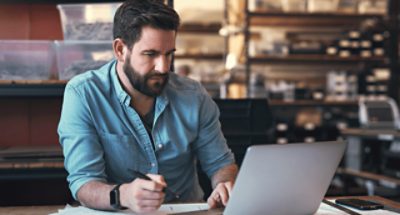 A person at a table taking notes and using a laptop.