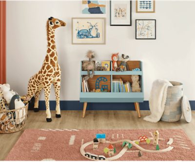 A playroom with earth tone paint and a wooden train set and large plush giraffe next to a cubby of books and toys.